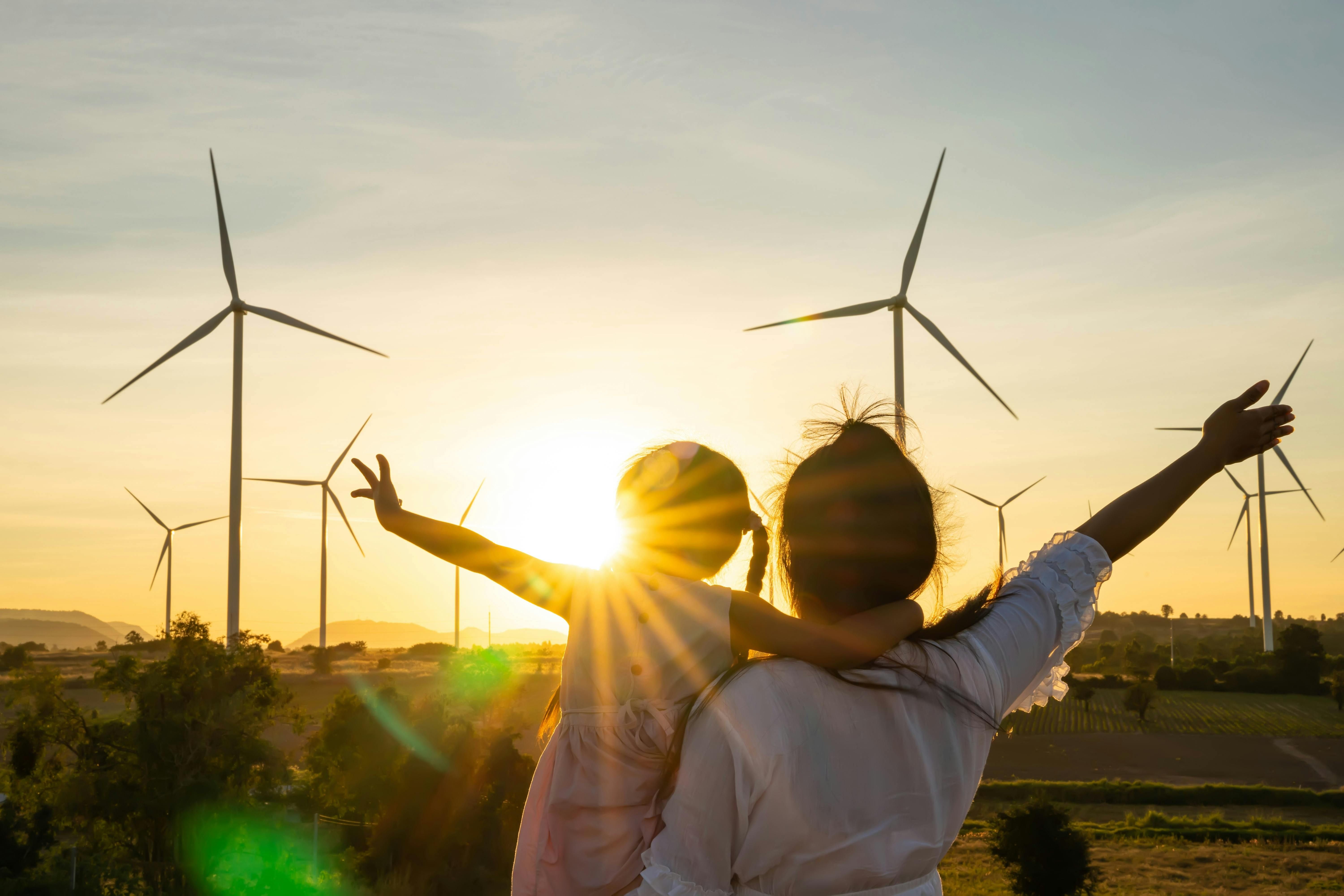 Woman and child looking over wind turbines with a sunset with arms spread open